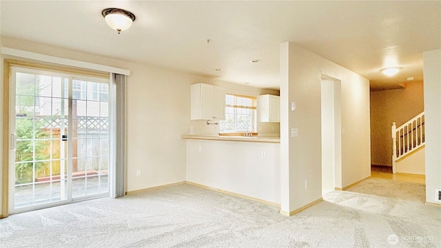 empty room with stairs, baseboards, a sink, and light colored carpet