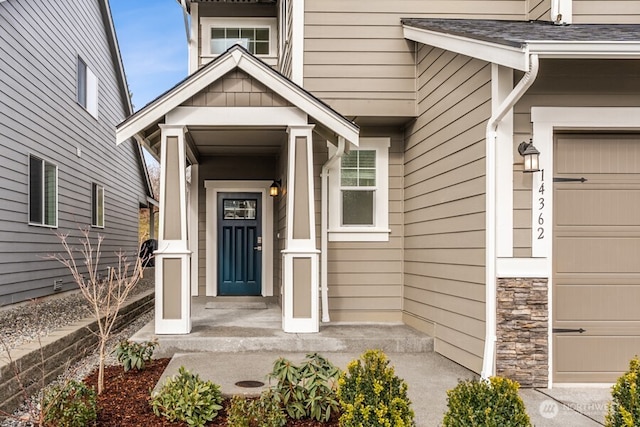 view of exterior entry with a shingled roof, stone siding, and a garage