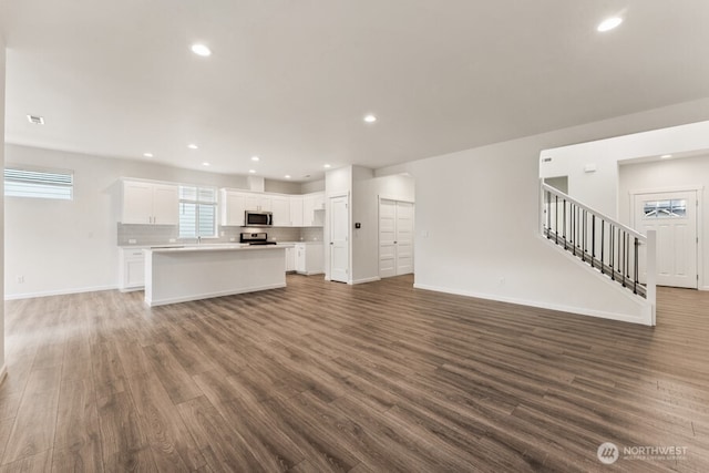 unfurnished living room featuring dark wood-type flooring, recessed lighting, baseboards, and stairs