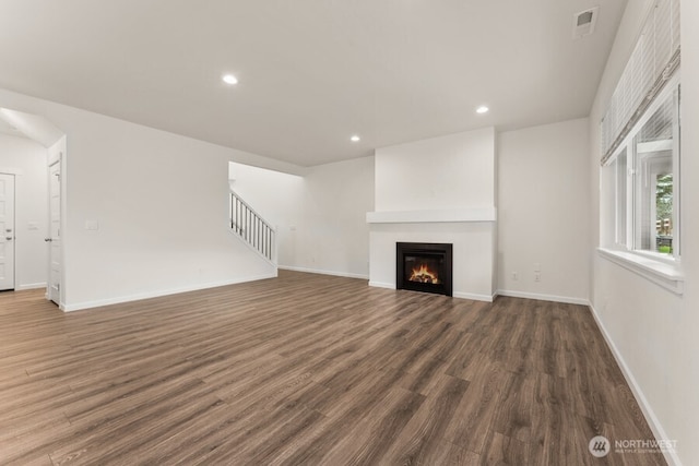 unfurnished living room with recessed lighting, wood finished floors, baseboards, stairway, and a glass covered fireplace