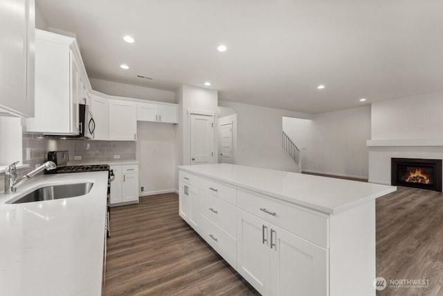 kitchen with stainless steel appliances, dark wood-style flooring, a sink, white cabinetry, and backsplash