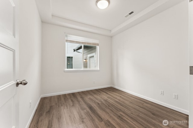 spare room with baseboards, visible vents, a raised ceiling, and wood finished floors