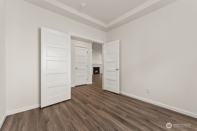 unfurnished bedroom featuring a lit fireplace, dark wood-type flooring, and baseboards