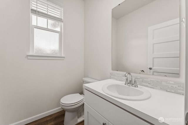 half bath featuring toilet, baseboards, wood finished floors, and vanity