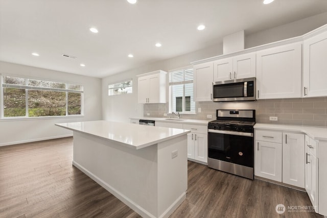 kitchen with appliances with stainless steel finishes, dark wood finished floors, a sink, and a center island