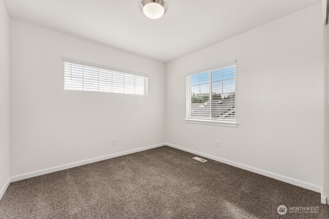 unfurnished room featuring dark colored carpet, visible vents, and baseboards