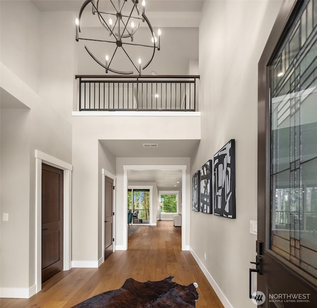 corridor with a high ceiling, baseboards, an inviting chandelier, and wood finished floors