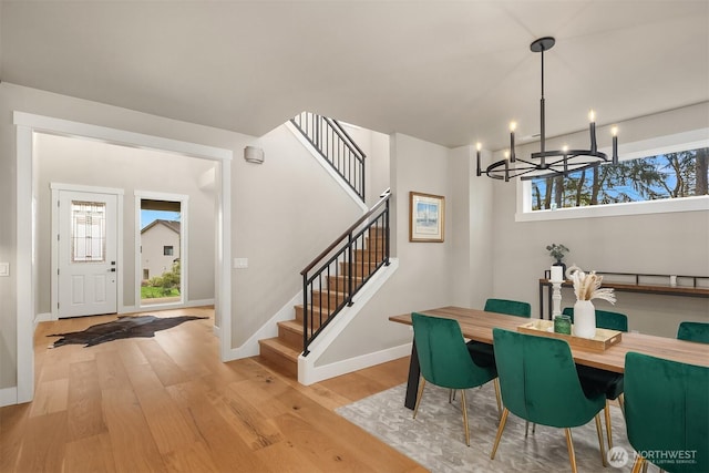 dining room with light wood-type flooring, baseboards, stairway, and a chandelier