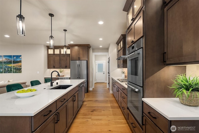 kitchen featuring light wood finished floors, glass insert cabinets, appliances with stainless steel finishes, dark brown cabinets, and a sink