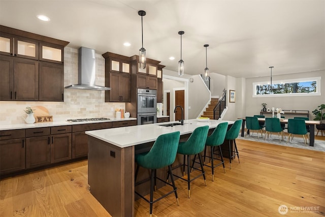 kitchen with light wood finished floors, wall chimney exhaust hood, appliances with stainless steel finishes, and a sink