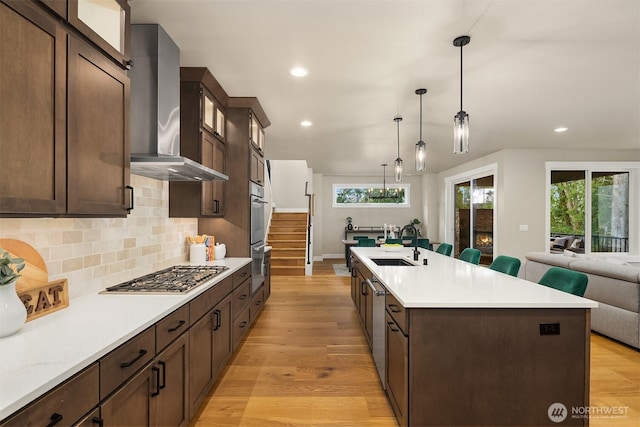 kitchen featuring light wood-type flooring, wall chimney exhaust hood, appliances with stainless steel finishes, and a sink