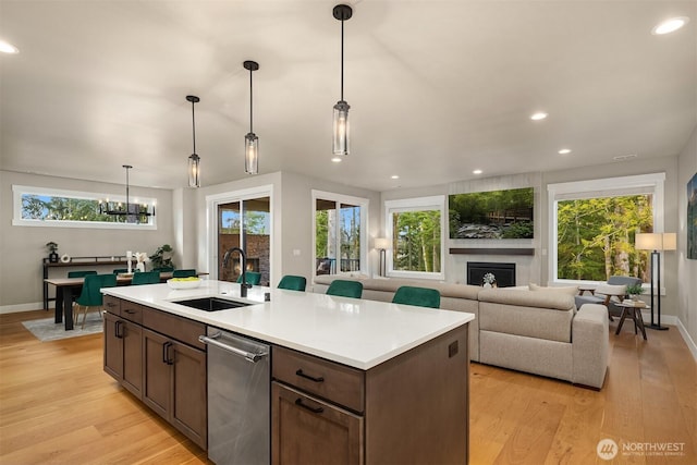 kitchen with light countertops, light wood-style flooring, a large fireplace, a sink, and dishwasher