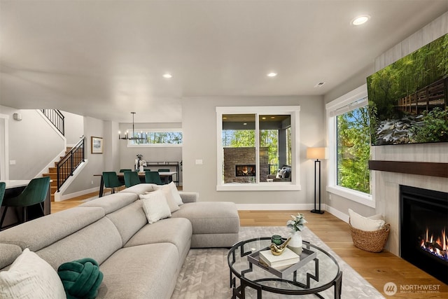 living area with a wealth of natural light, a lit fireplace, stairs, and wood finished floors