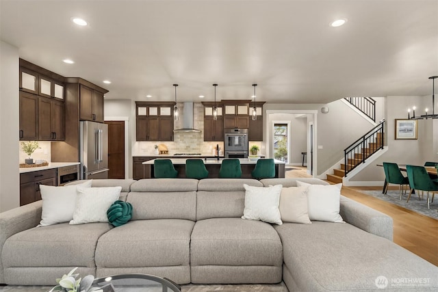 living area with light wood-style flooring, recessed lighting, stairway, and an inviting chandelier