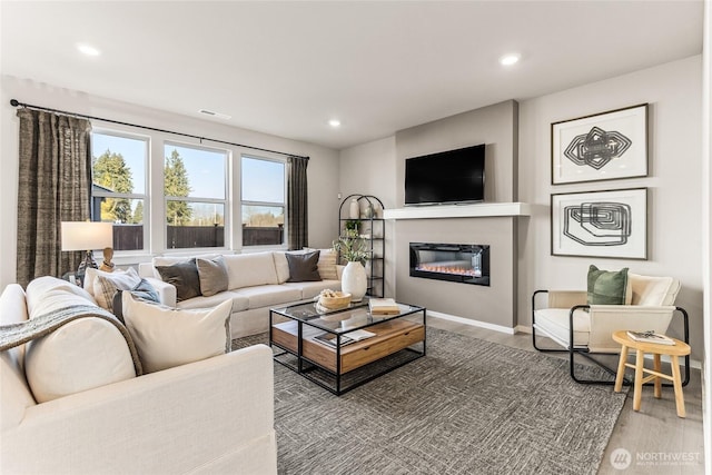 living room featuring visible vents, baseboards, a glass covered fireplace, wood finished floors, and recessed lighting