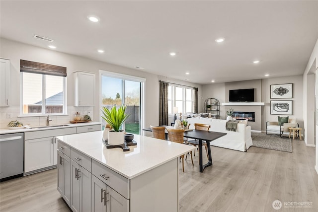 kitchen with a sink, visible vents, backsplash, dishwasher, and a glass covered fireplace