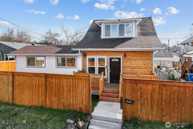 view of front of home with a deck, roof with shingles, and fence