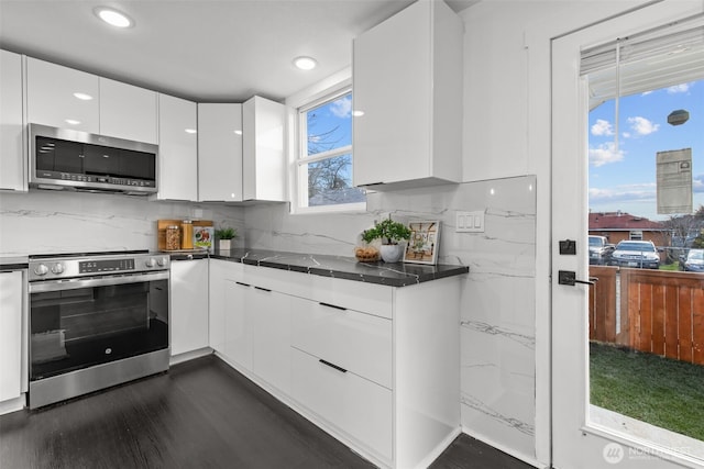 kitchen with dark countertops, backsplash, appliances with stainless steel finishes, white cabinetry, and modern cabinets