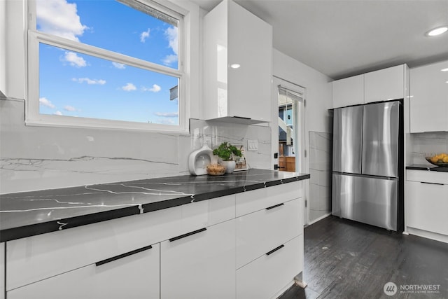 kitchen with white cabinets, dark countertops, dark wood-type flooring, freestanding refrigerator, and backsplash