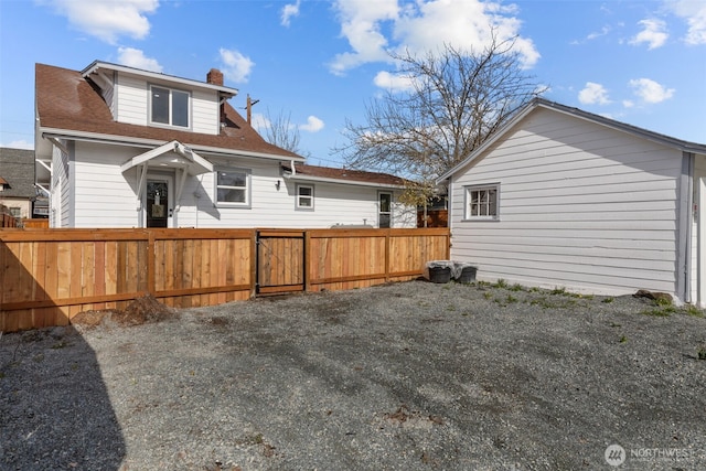 back of house featuring a shingled roof, a chimney, and fence