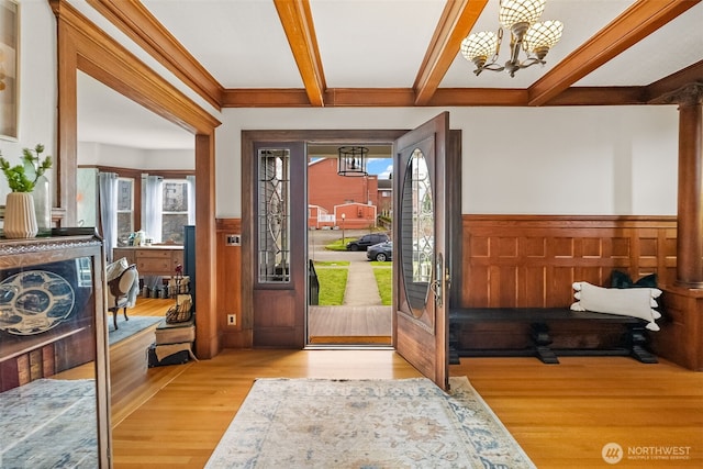 foyer entrance with plenty of natural light, beamed ceiling, a notable chandelier, and wainscoting