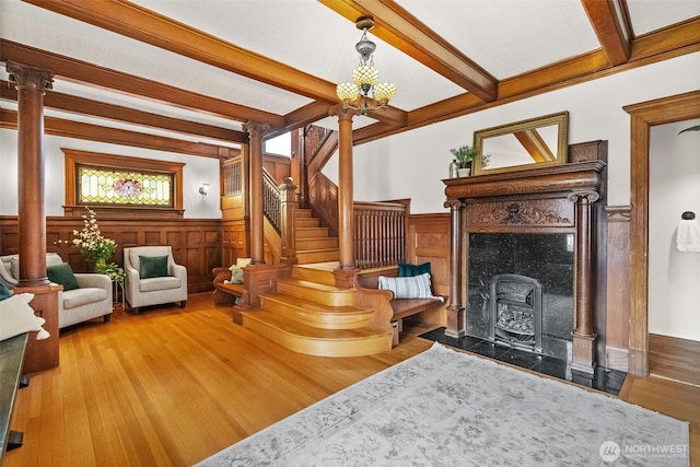 living area featuring ornate columns, stairway, beamed ceiling, and wood finished floors