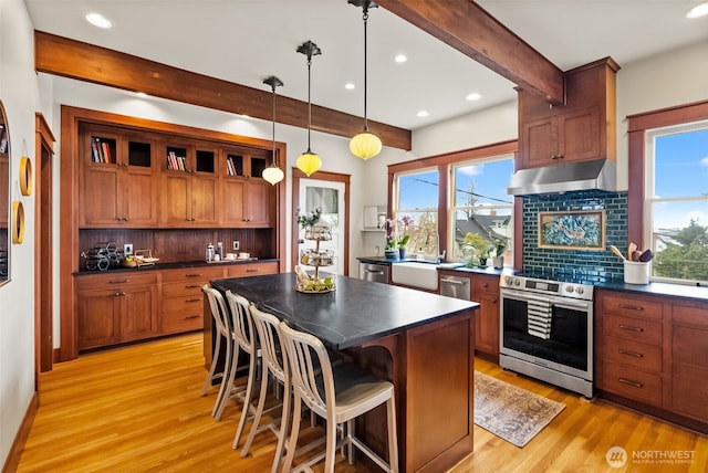 kitchen featuring beam ceiling, stainless steel appliances, dark countertops, light wood-type flooring, and under cabinet range hood