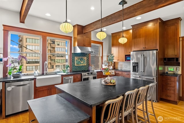 kitchen featuring under cabinet range hood, stainless steel appliances, a sink, beam ceiling, and dark countertops