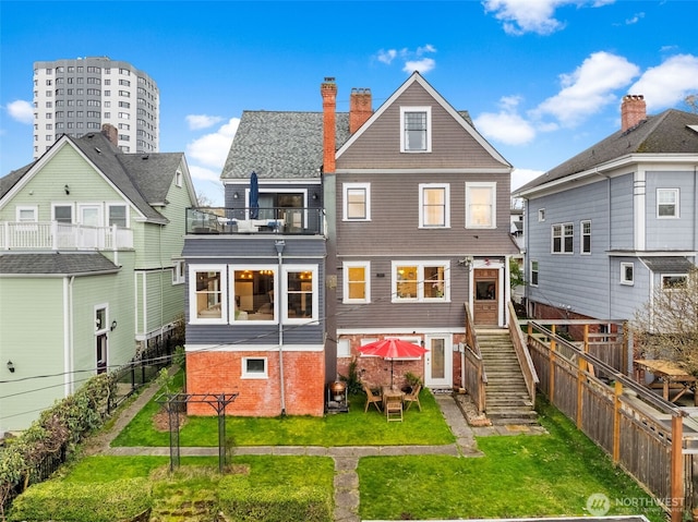 back of house featuring a fenced backyard, a balcony, a yard, stairway, and a chimney