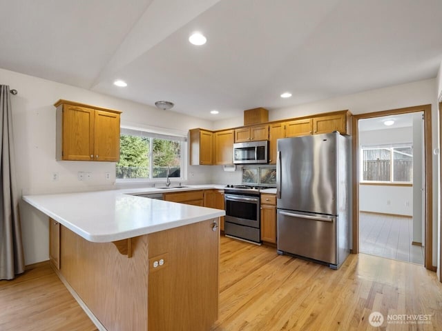 kitchen with light countertops, appliances with stainless steel finishes, a peninsula, light wood-style floors, and a sink