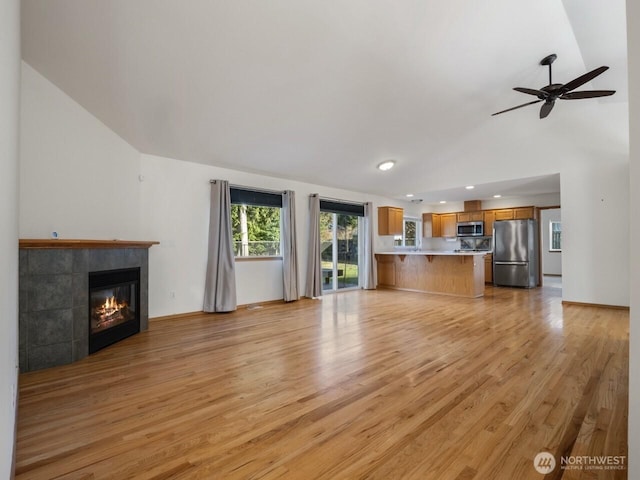 unfurnished living room featuring ceiling fan, lofted ceiling, light wood-style flooring, and a tile fireplace