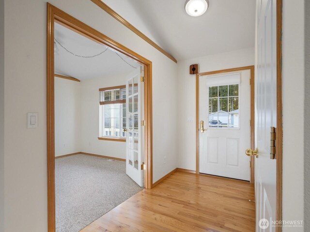 entryway with a healthy amount of sunlight, light colored carpet, light wood-style flooring, and baseboards