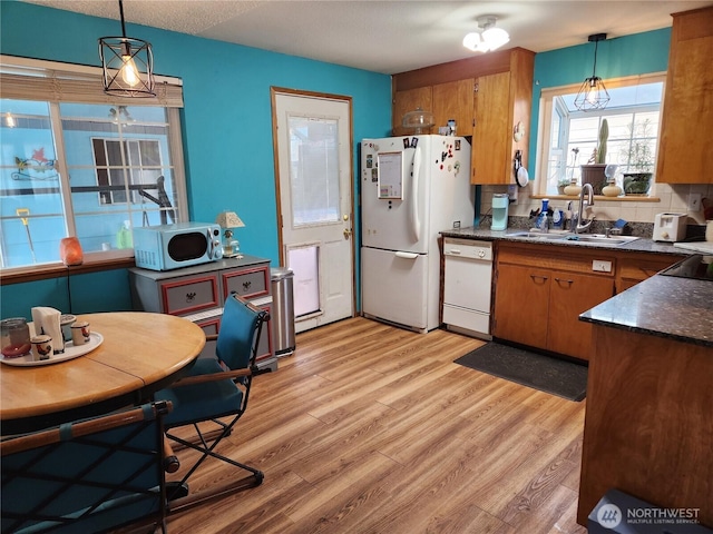 kitchen with dark countertops, brown cabinets, white appliances, and a sink