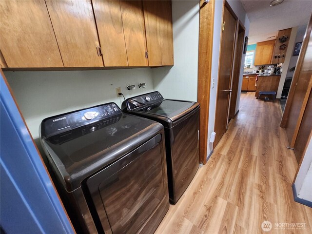 clothes washing area with cabinet space, separate washer and dryer, and light wood finished floors