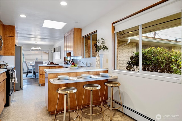 kitchen featuring brown cabinets, freestanding refrigerator, a chandelier, black range with electric cooktop, and a peninsula