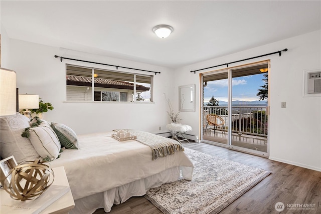 bedroom featuring a wall unit AC, a baseboard heating unit, wood finished floors, baseboards, and access to outside