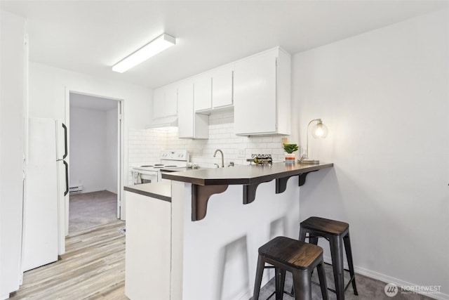 kitchen featuring white appliances, decorative backsplash, white cabinetry, dark countertops, and a kitchen breakfast bar