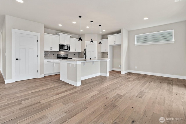 kitchen with light wood-style floors, tasteful backsplash, stainless steel appliances, and light countertops