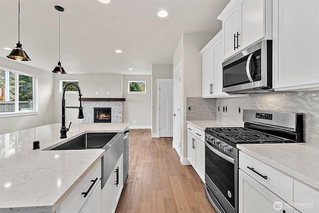 kitchen featuring light wood finished floors, decorative backsplash, a glass covered fireplace, appliances with stainless steel finishes, and white cabinetry