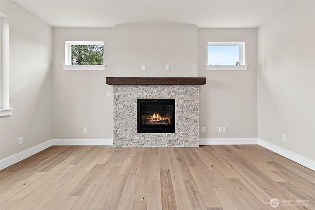 unfurnished living room with a stone fireplace, plenty of natural light, wood finished floors, and baseboards