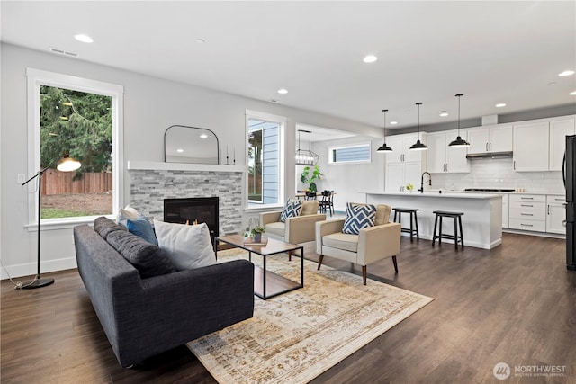 living room with a stone fireplace, dark wood-type flooring, visible vents, and baseboards