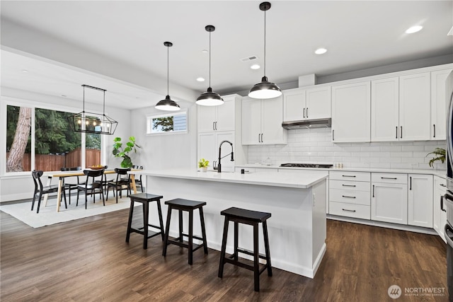 kitchen featuring dark wood-style flooring, light countertops, under cabinet range hood, and gas cooktop