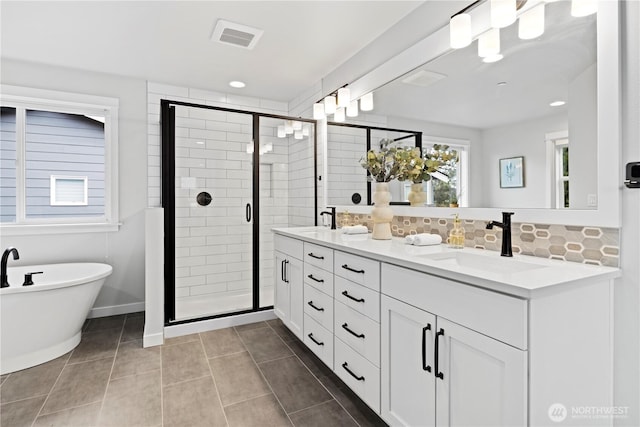 bathroom with double vanity, a stall shower, tasteful backsplash, a freestanding bath, and a sink