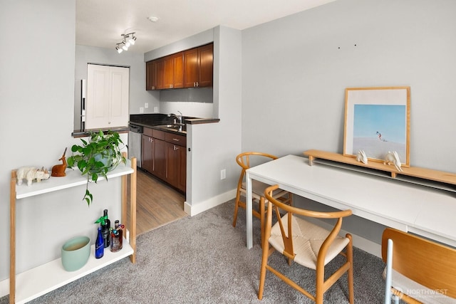 kitchen with a sink, carpet flooring, baseboards, stainless steel dishwasher, and dark countertops