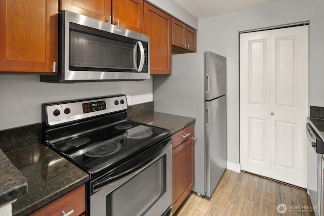 kitchen with dark stone counters, appliances with stainless steel finishes, brown cabinetry, and light wood-style flooring