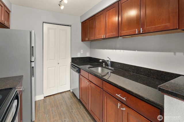 kitchen featuring appliances with stainless steel finishes, light wood-type flooring, a sink, and dark stone countertops