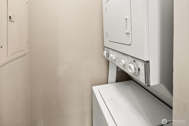 laundry room with laundry area, a textured wall, stacked washer / dryer, and electric panel