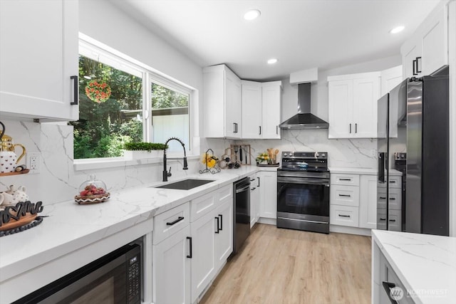 kitchen with stainless steel appliances, white cabinetry, a sink, and wall chimney range hood