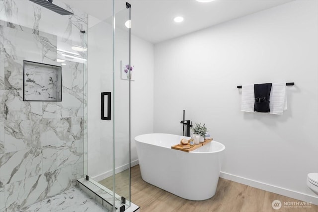 full bath with wood finished floors, a freestanding tub, a marble finish shower, and baseboards