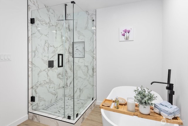 full bath featuring wood finished floors, a soaking tub, a marble finish shower, and baseboards